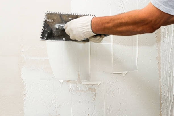 A man uses a trowel to apply paint on a wall, demonstrating drywall repair near me