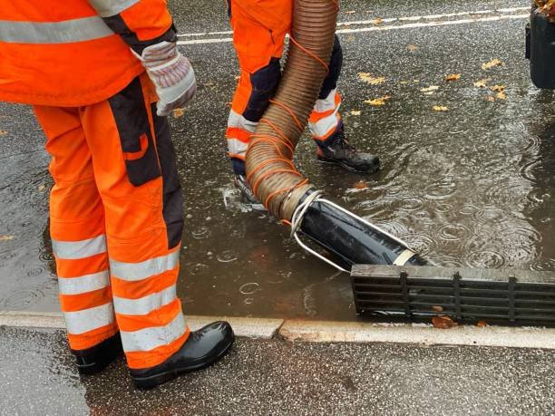 Two men in orange work clothes stand in a puddle, engaged in flood cleanup services.