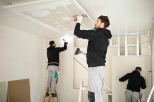 Two men repairing a water-damaged ceiling in a room, focused on restoring the structure.
