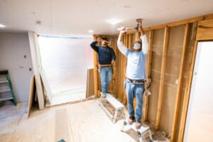 Two men repairing a wall in a room as part of a water damage restoration project.