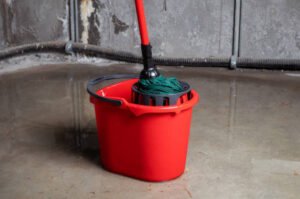 A red mop bucket and a green bucket, tools for cleaning a flooded basement.
